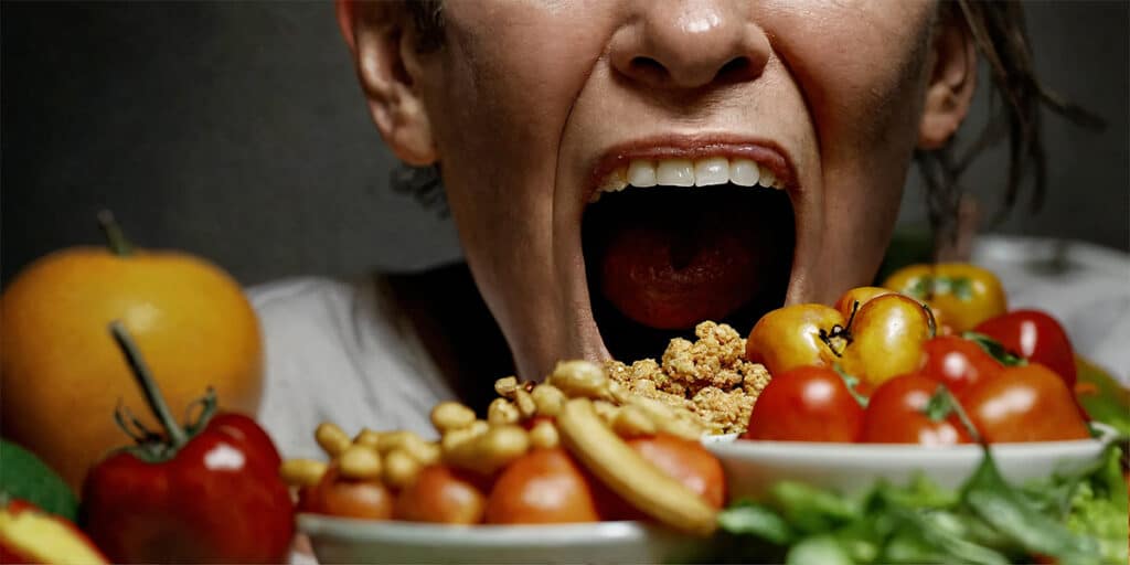 A person with an open mouth showcasing increased saliva, with saliva-stimulating foods like citrus and ginger in the foreground.