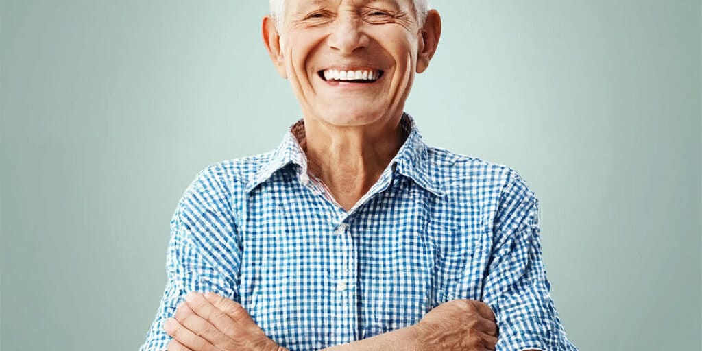 Senior with a bright, healthy smile standing confidently with arms folded, embodying oral wellness.